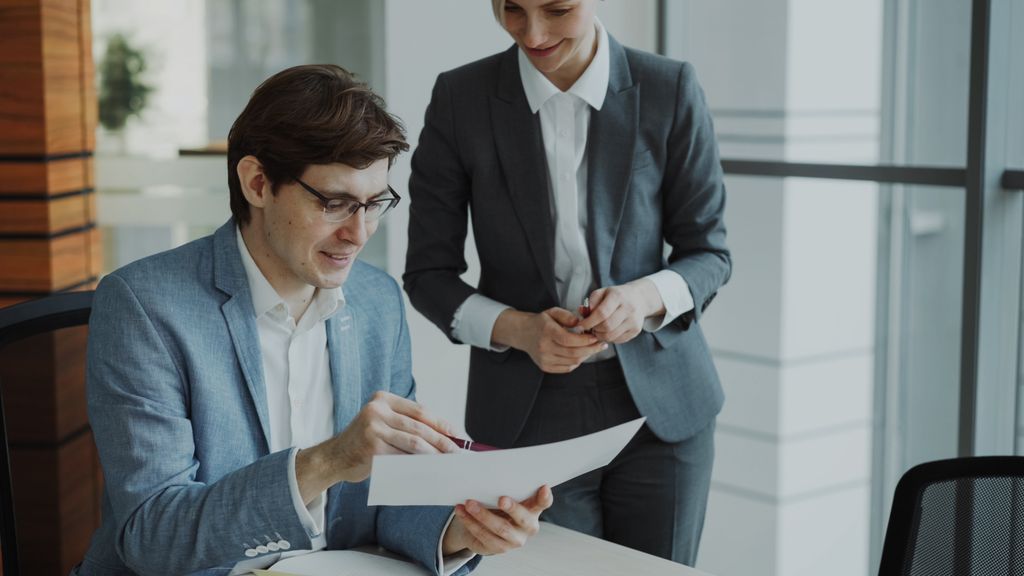 Two business professionals discussing a document in a modern office setting.